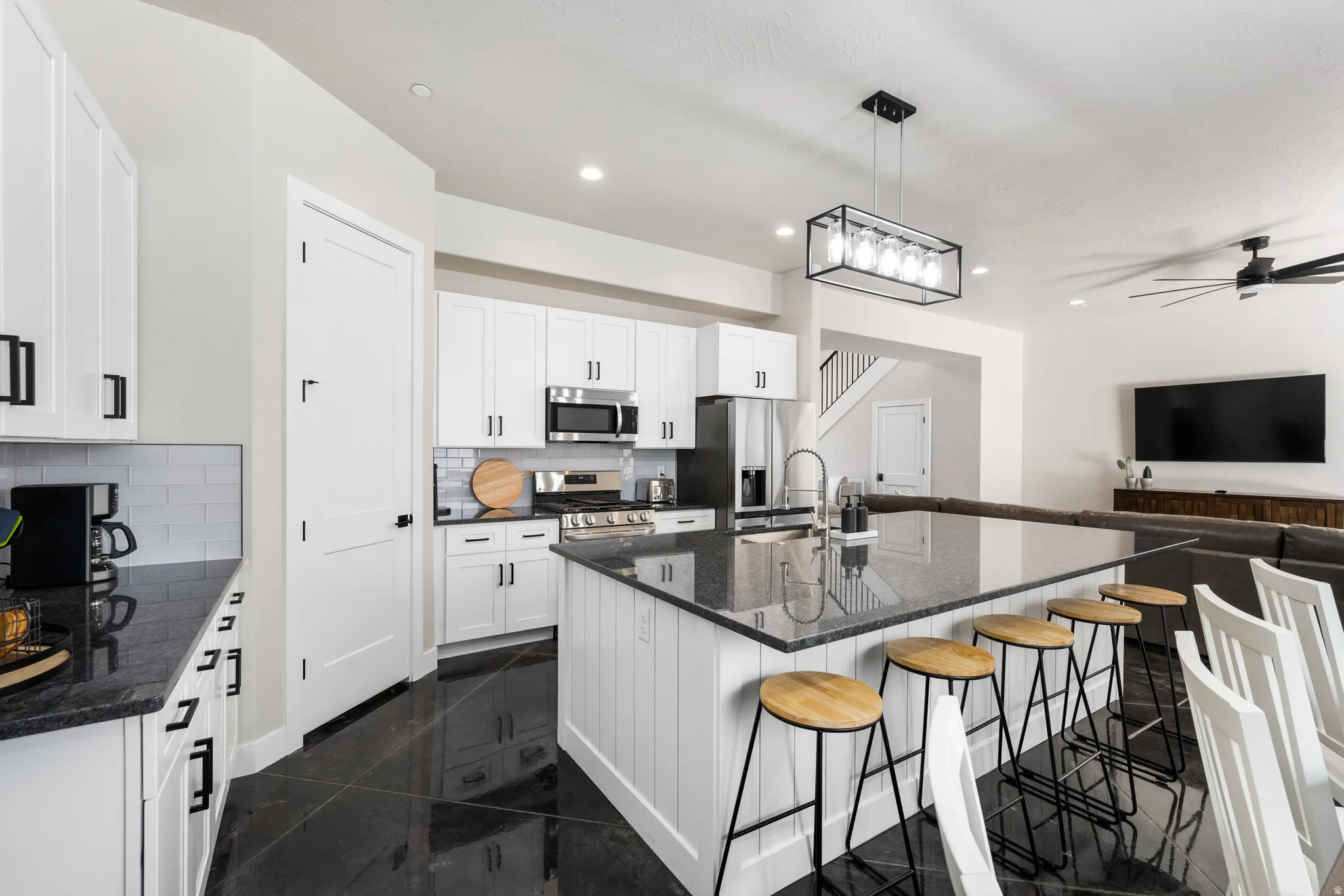 Modern kitchen with white cabinetry and dark countertops, featuring a large island with seating