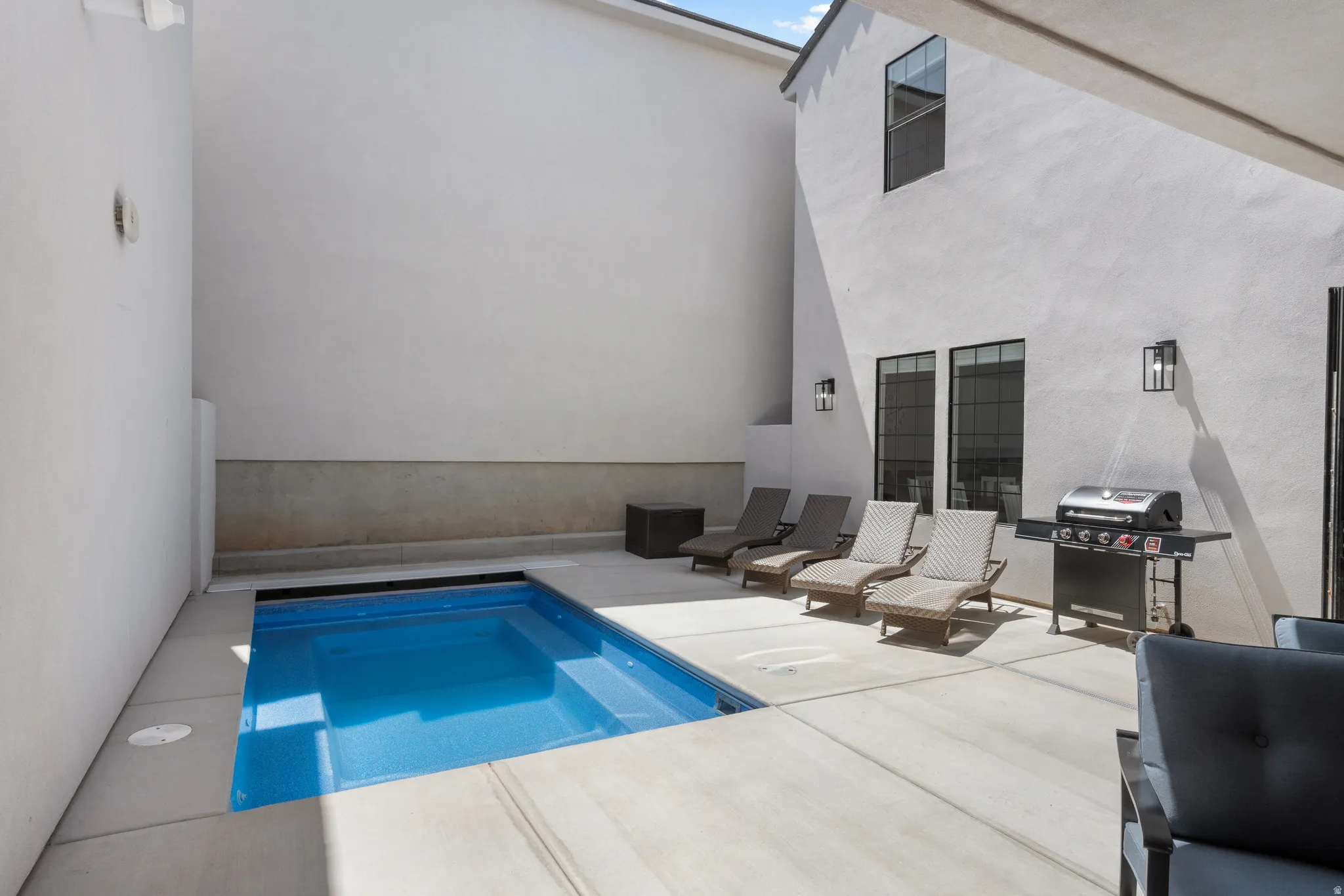 Outdoor courtyard featuring a built-in swimming pool with an integrated spa, surrounded by light-toned concrete hardscaping