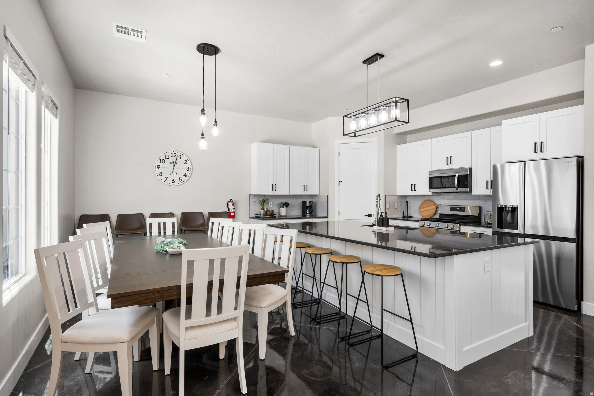 Open-concept kitchen and dining area featuring a large center island with counter seating, stainless steel appliances, white cabinetry with dark hardware, and dark flooring