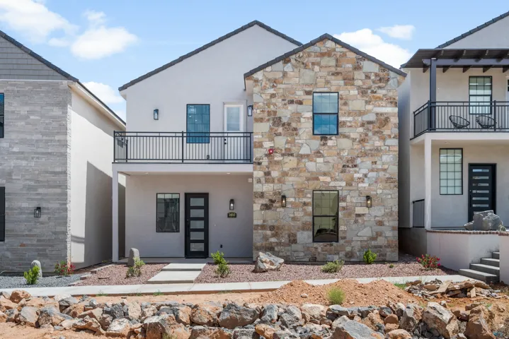 Contemporary exterior featuring a stone façade, stucco finishes, a second-story balcony with iron railing, a dark entry door with frosted glass panels, and exterior sconce lighting
