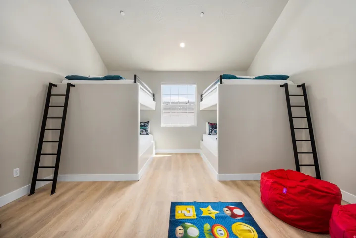 Room featuring built-in bunk beds with black ladders, light wood-finish flooring, and a single window