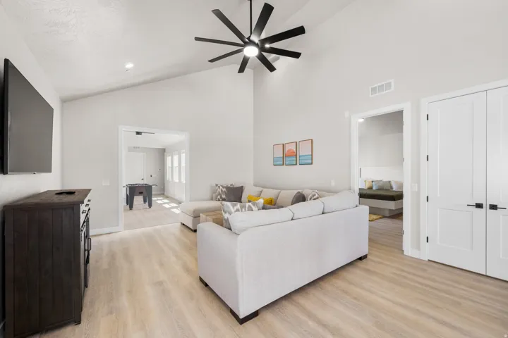 Bright living area with vaulted ceilings, a large black ceiling fan, and light wood-finish flooring