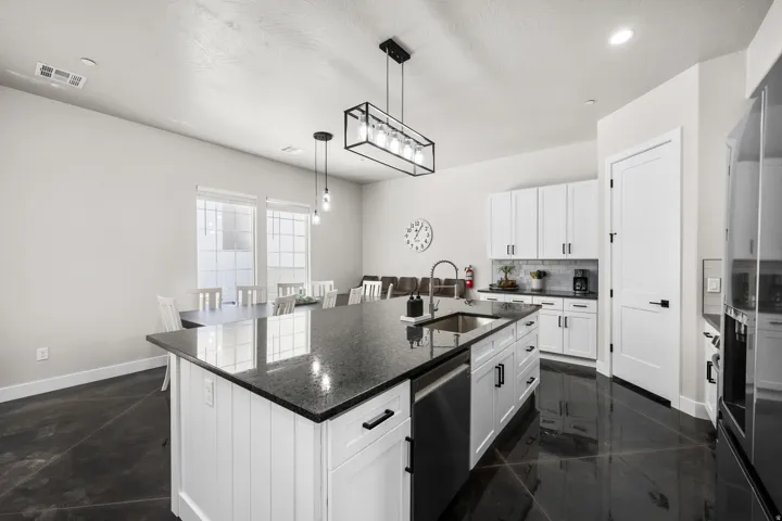 Open-concept kitchen featuring a large island with a sink, white cabinetry, dark countertops, and stainless steel appliances