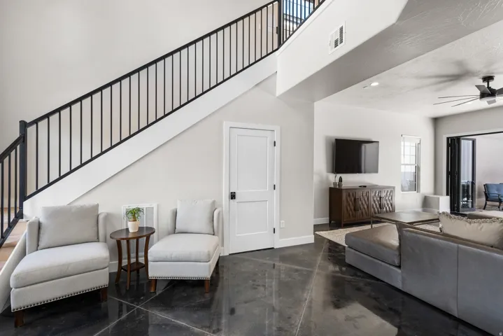 Open-concept living space featuring a modern staircase with dark metal railings, polished dark flooring, and a ceiling fan