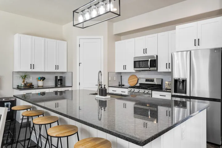 Spacious kitchen featuring a large island with a dark countertop, white shaker-style cabinetry, stainless steel appliances, a tile backsplash, and a modern linear chandelier