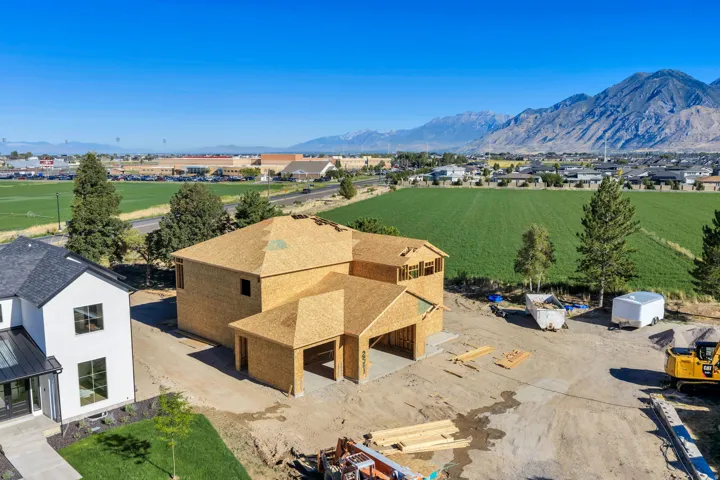 Under construction residential structure with a shingled roof, mountain backdrop, and a field extending into the distance