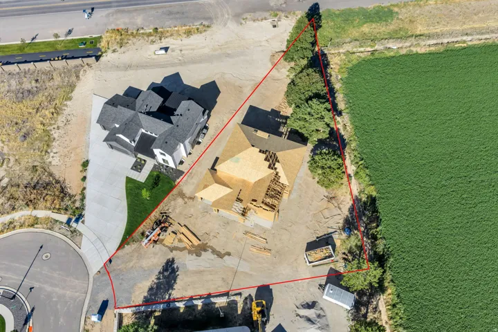 New construction framing, extensive lot, adjacent finished property, paved street access, and surrounding green fields