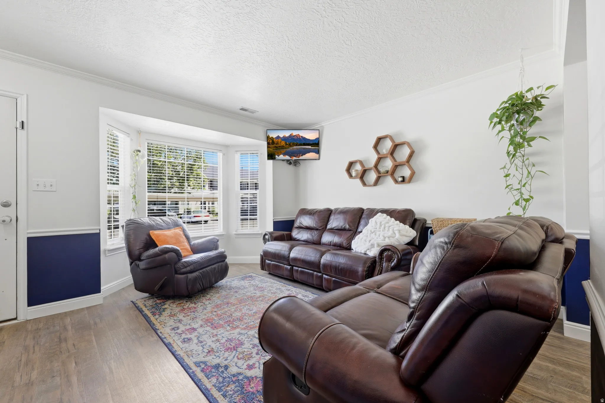 Living area featuring wood-finish flooring, a bay window with blinds, two-tone wall paint, and crown molding
