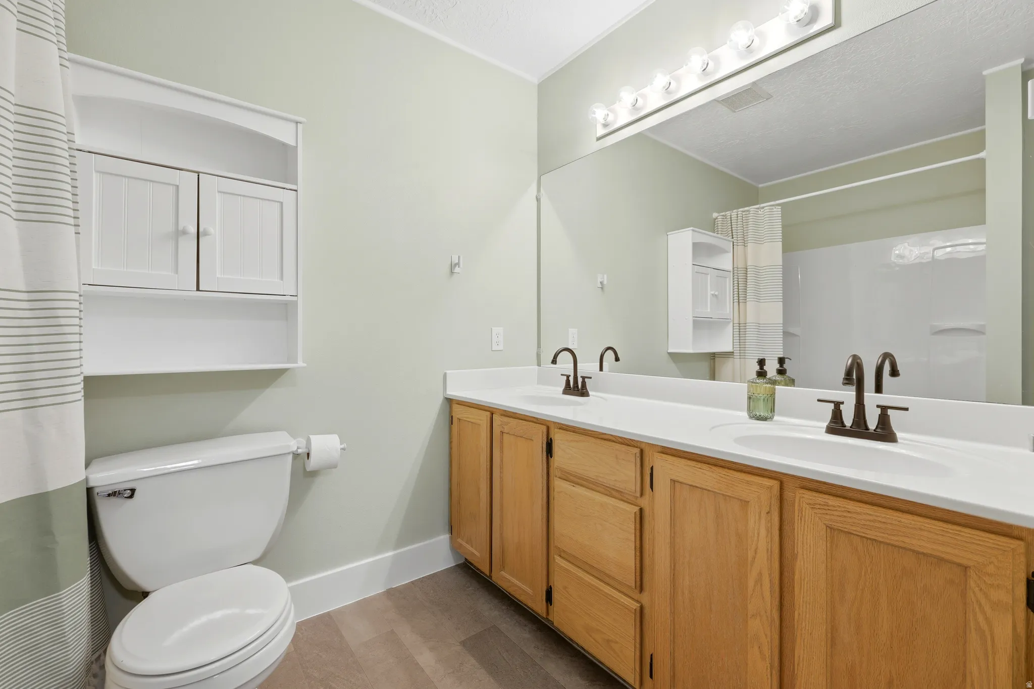 Bathroom featuring a dual vanity with light wood cabinetry, white countertops, and bronze-finish faucets