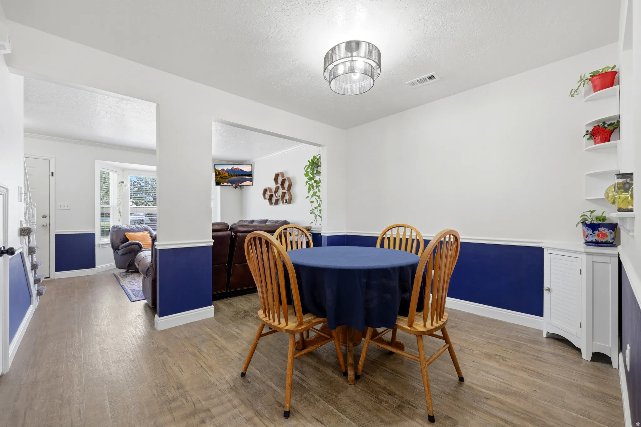 Open-concept living area with wood-finish flooring, two-tone wall paint, a bay window, and a built-in corner cabinet with shelving