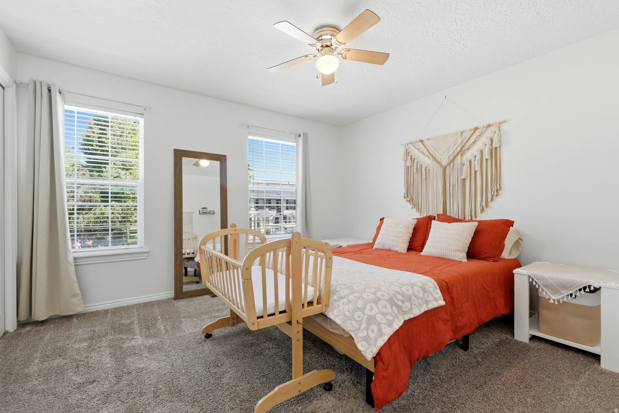 Bright room featuring two large windows with blinds and drapes, a ceiling fan with integrated lighting, and neutral carpeting