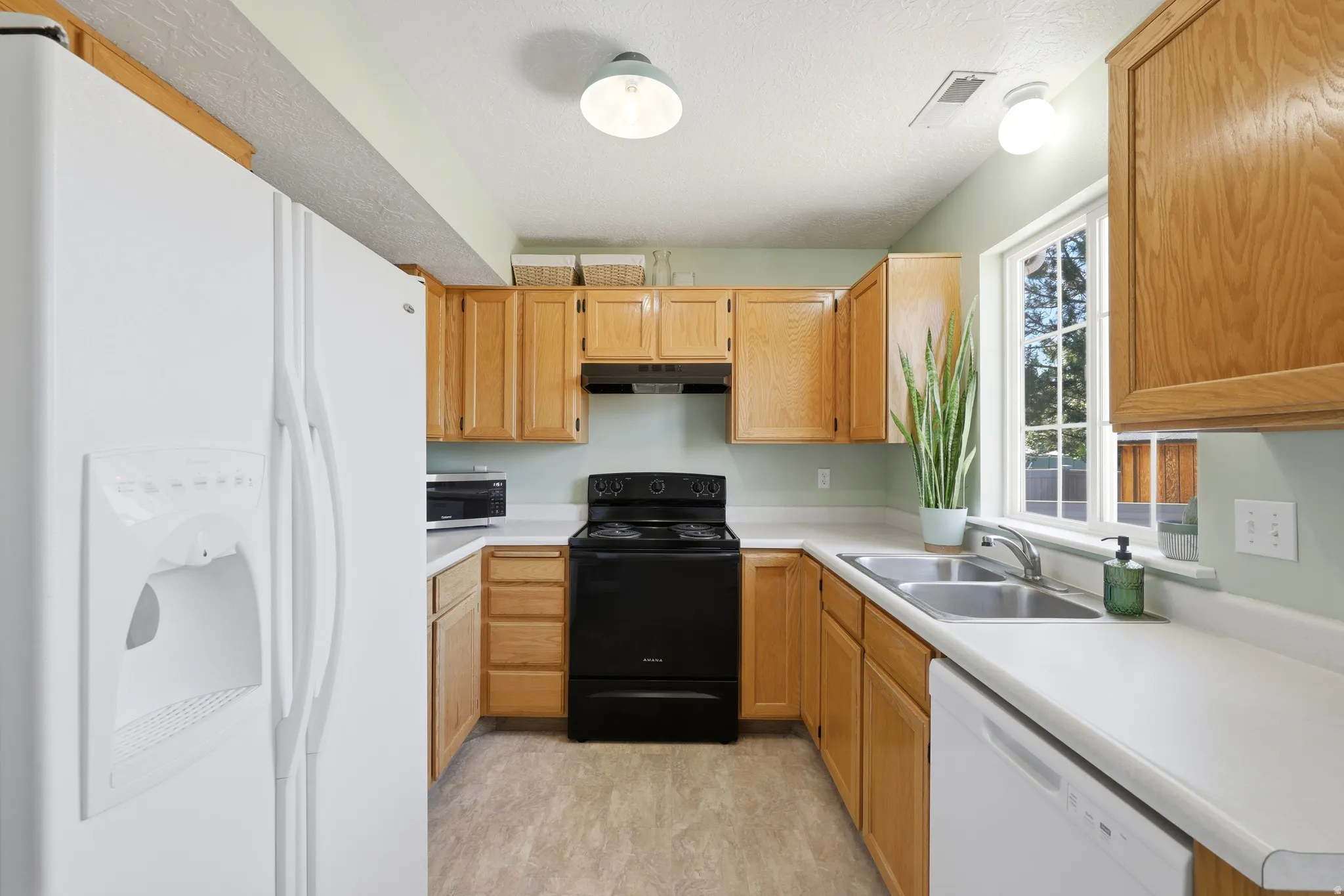 Kitchen featuring light wood cabinetry, white countertops, a double basin stainless steel sink, black electric range, and a white dishwasher