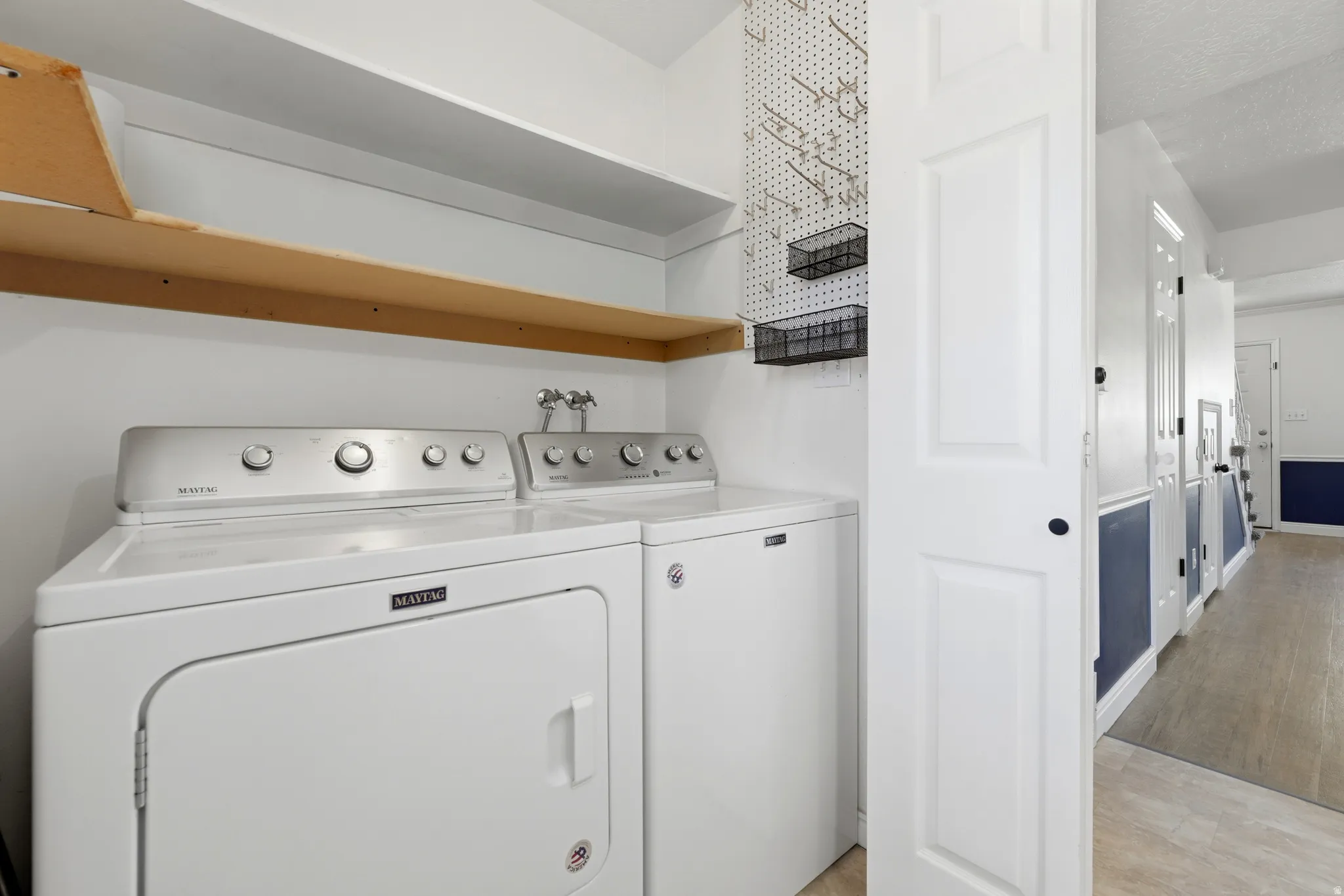 Dedicated laundry area featuring a washer and dryer, an overhead wooden shelf, and a white pegboard