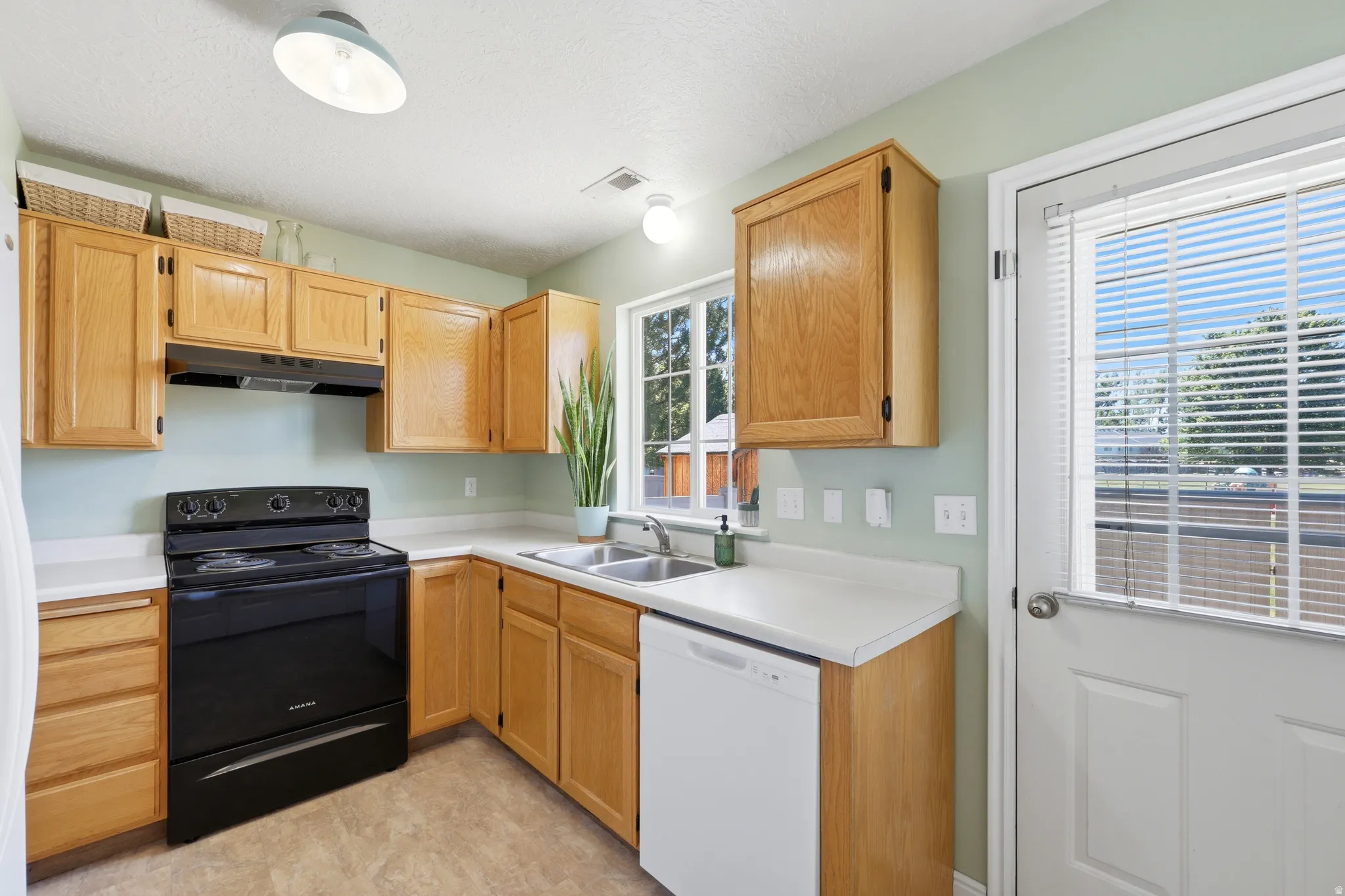 Kitchen featuring light wood cabinetry, white countertops, a double basin sink, and wood-finish flooring