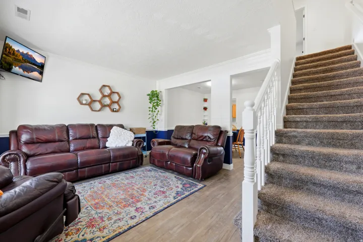 Living space featuring wood-finish flooring, a carpeted staircase with white balusters and newel post, and white crown molding