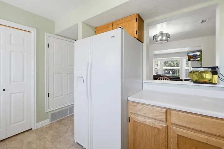 Kitchen area featuring light wood-finish cabinetry, white countertop, and pass-through window to an adjacent room
