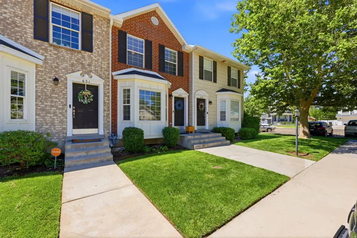 Two-story townhouse exterior with a mix of brick and siding, featuring bay windows, black shutters, and individual front entrances with concrete steps