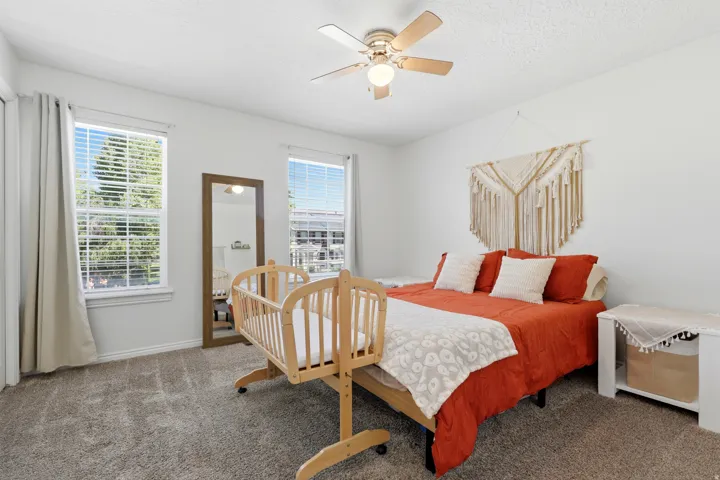 Bright room featuring two large windows with blinds and drapes, a ceiling fan with integrated lighting, and neutral carpeting