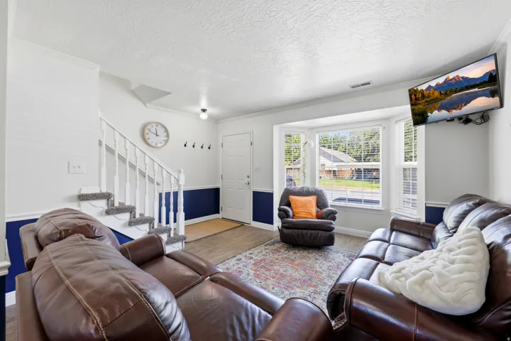 Inviting living area featuring a bay window, wood-finish flooring, a white staircase with carpeted treads, and a contrasting two-tone wall treatment