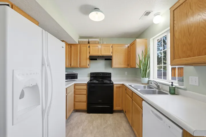 Kitchen featuring light wood cabinetry, white countertops, a double basin stainless steel sink, black electric range, and a white dishwasher
