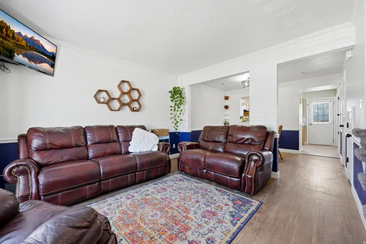 Living area featuring wood-finish flooring, white walls with a blue wainscoting detail, crown molding, and a visible doorway