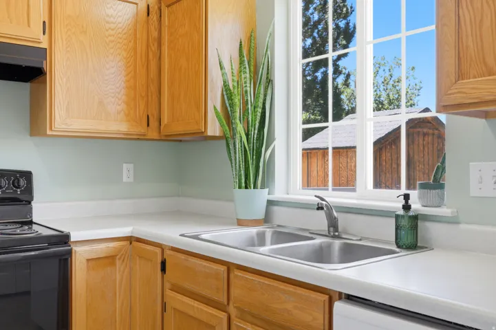 Kitchen featuring natural wood cabinetry, light-toned countertops, a double basin stainless steel sink, and a black electric range with an overhead microwave
