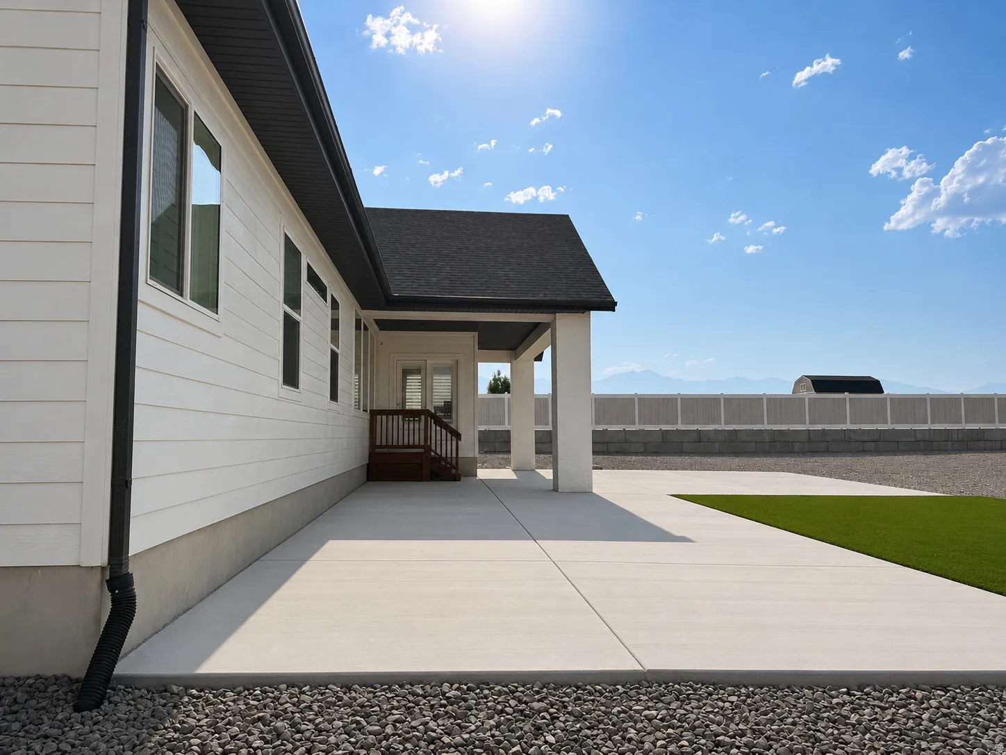 Spacious concrete patio with artificial turf accent, leading to a covered porch with wooden stairs and railing