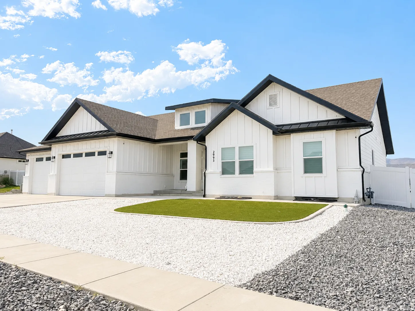 Modern farmhouse-style exterior featuring white vertical siding, dark trim, a two-car garage, a gravel driveway, and a manicured lawn