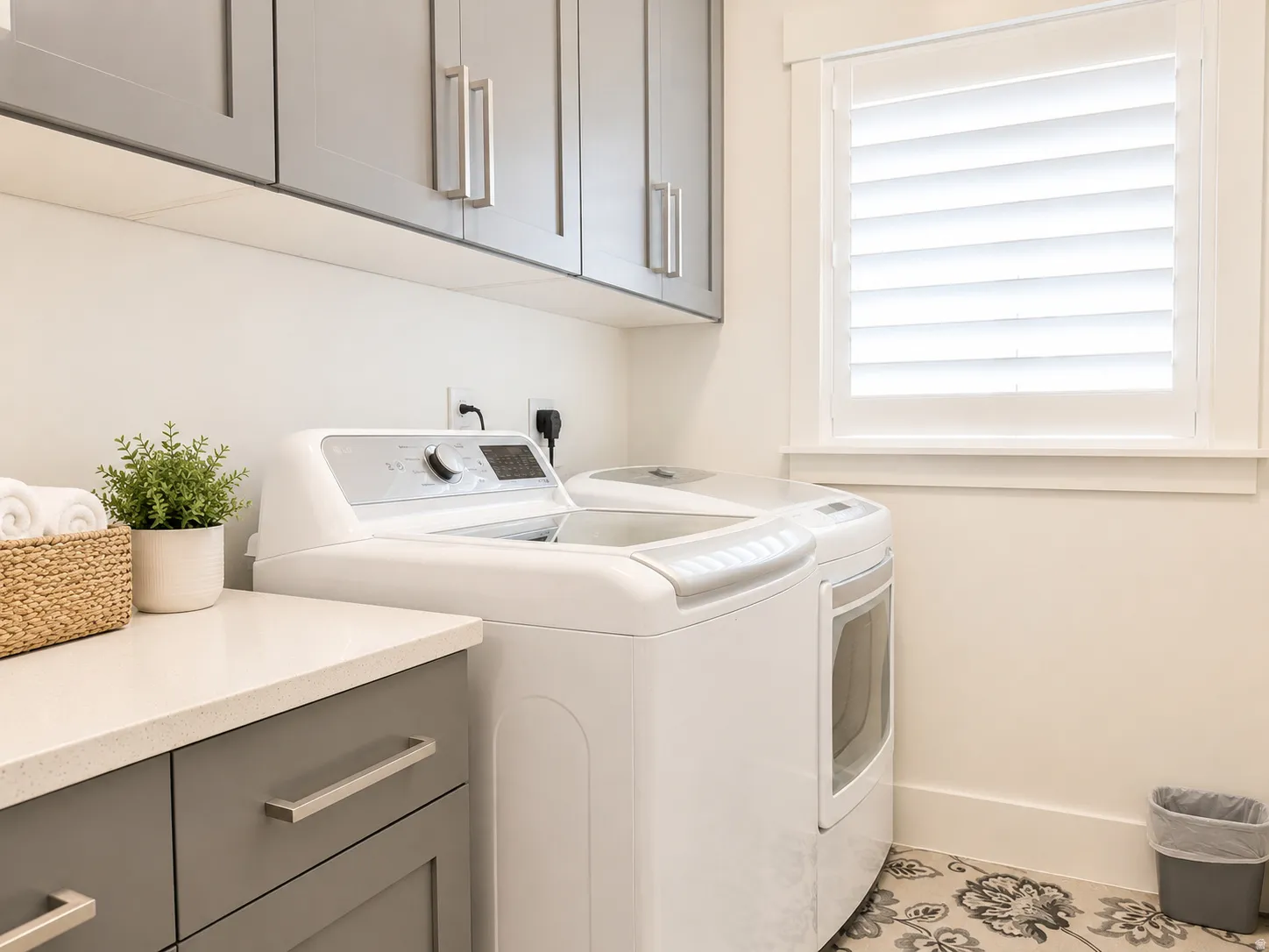 Laundry area featuring grey shaker-style cabinetry, a light-toned countertop, and a window with white plantation shutters