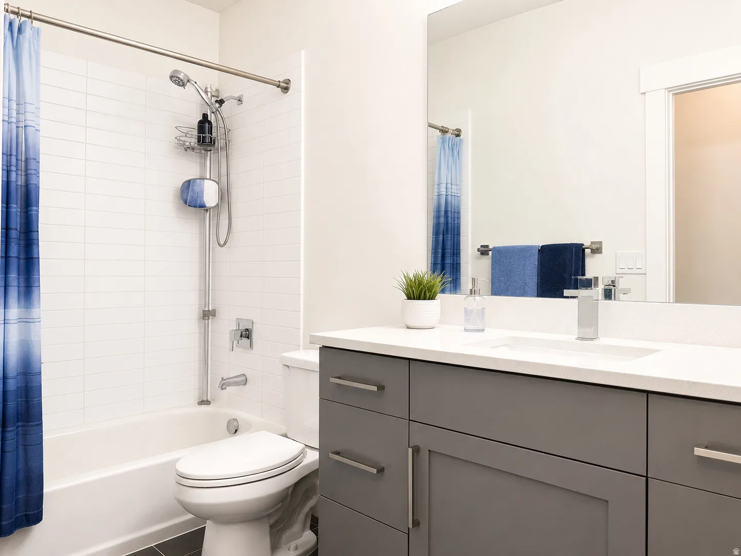 Contemporary bathroom featuring a tub/shower combination with white subway tile surround, a sleek toilet, a gray vanity with shaker-style cabinetry, and a countertop with an integrated sink and chrome faucet