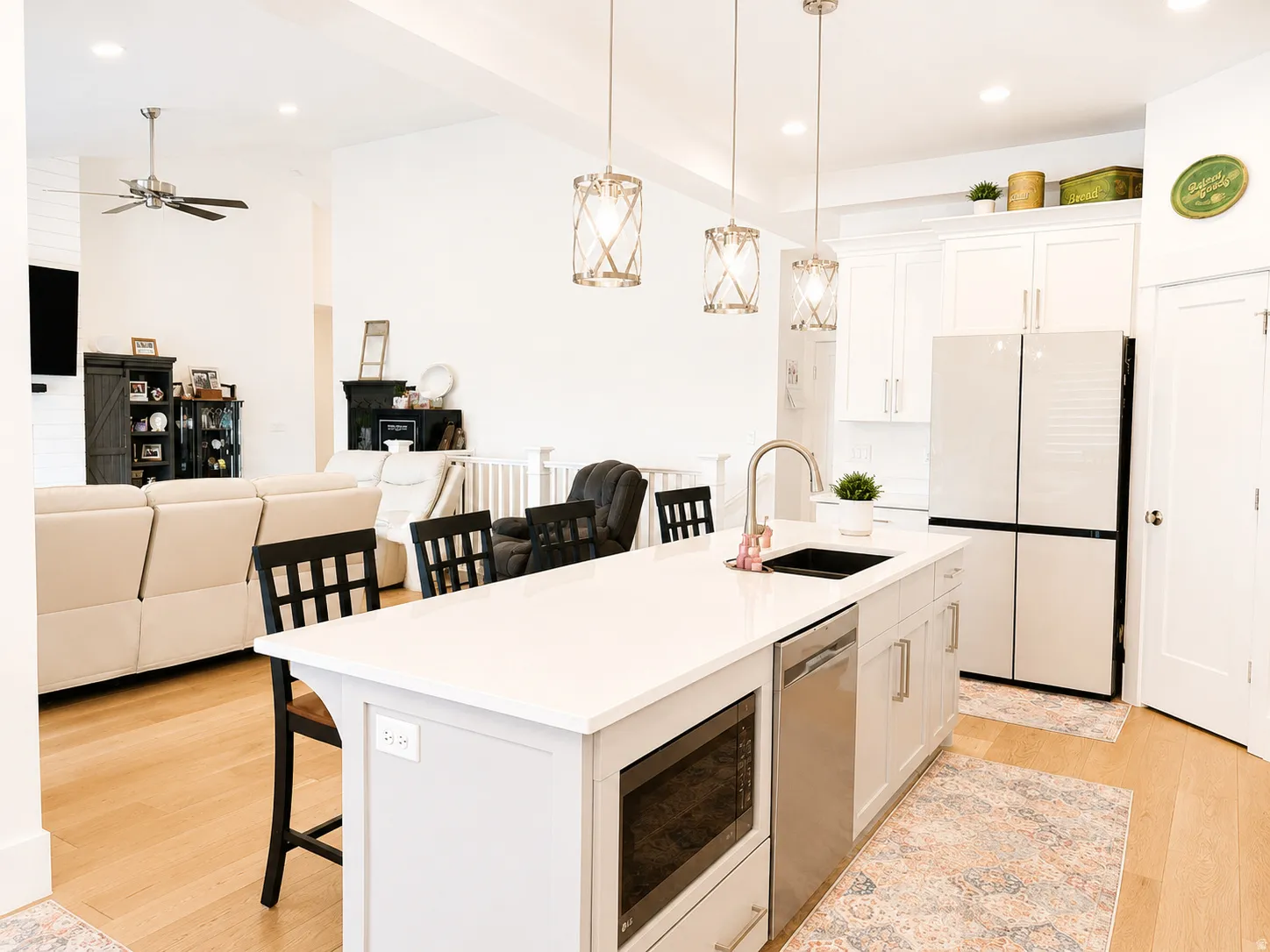 Spacious kitchen featuring a central island with integrated sink and dishwasher, white cabinetry, a built-in microwave, and wood-finish flooring