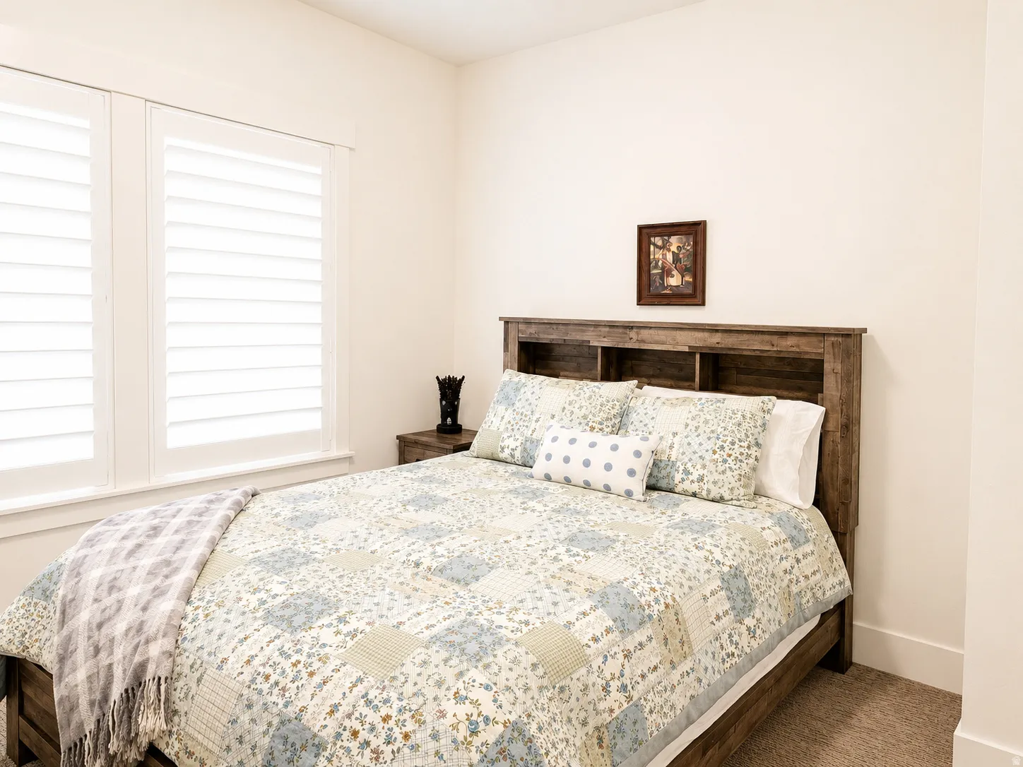Bedroom featuring white plantation shutters, a wood-finish headboard with integrated shelving, and neutral carpeting