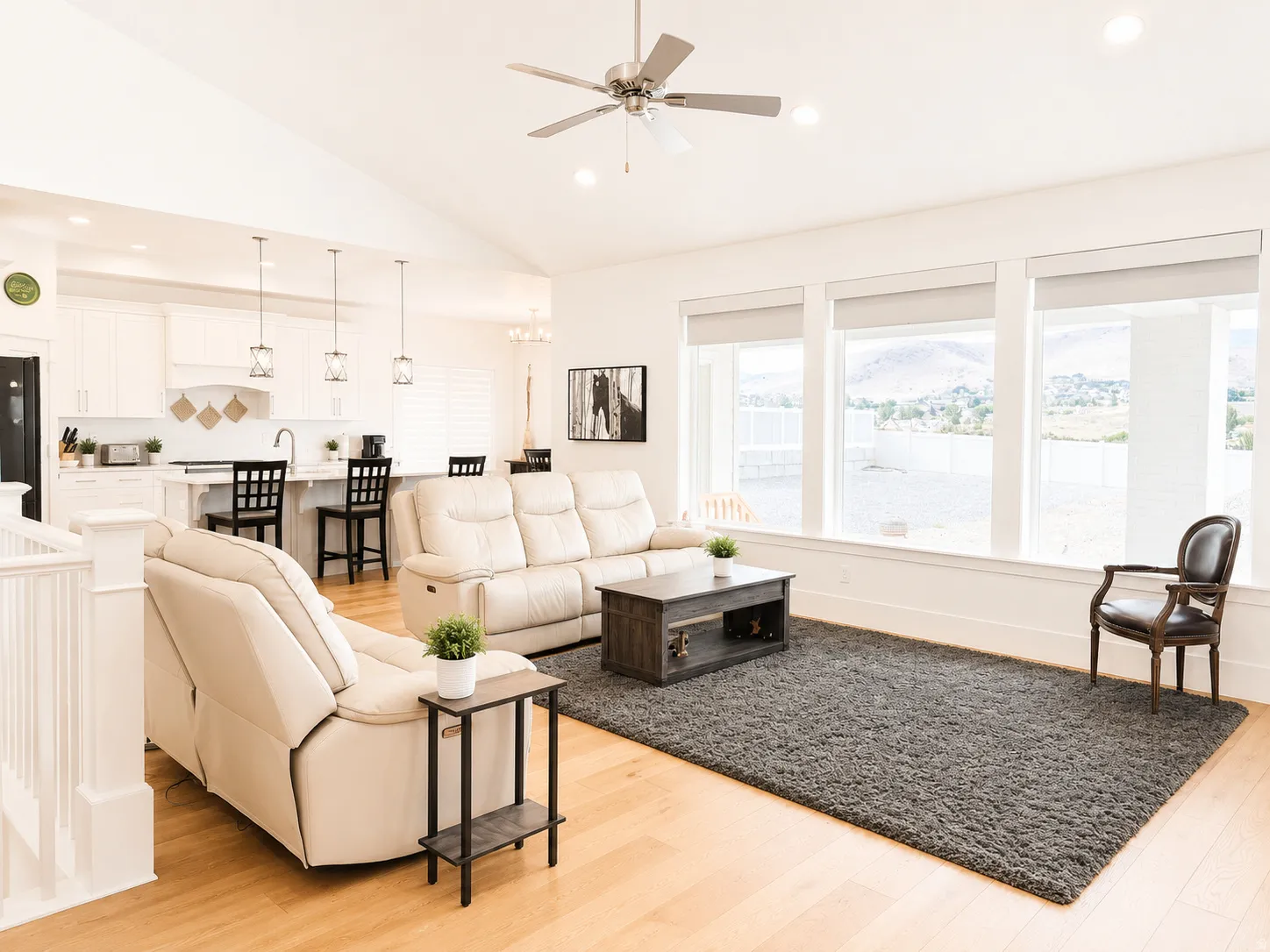 Open-concept living space featuring vaulted ceilings, light wood-finish flooring, and a kitchen with white cabinetry and a breakfast bar