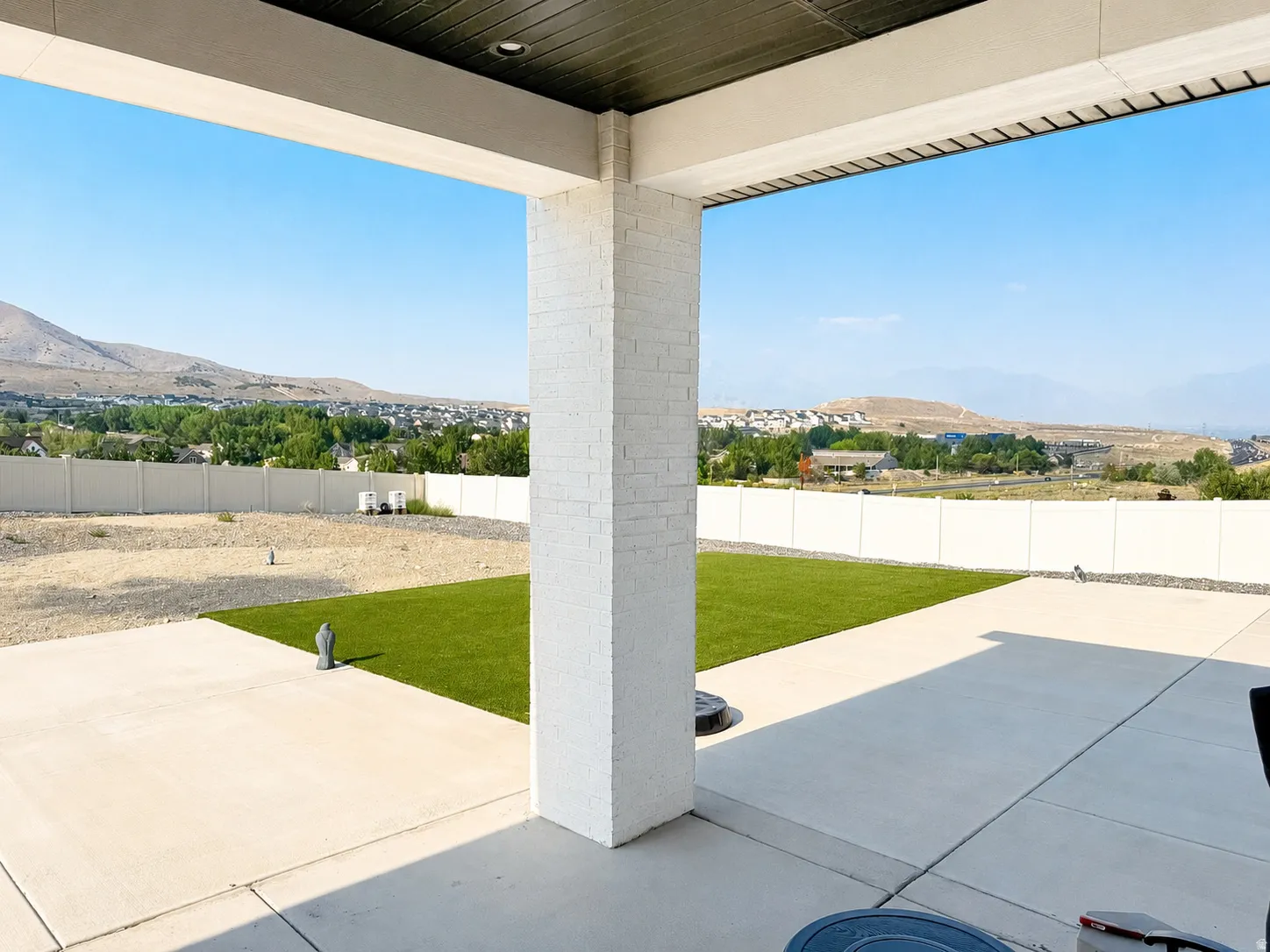 Expansive covered patio featuring a concrete surface, white brick pillar, and a dark wood-finish ceiling