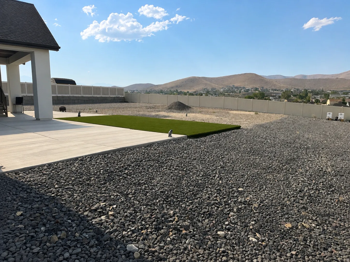 Expansive outdoor space featuring a concrete patio, a strip of artificial turf, and extensive gravel landscaping