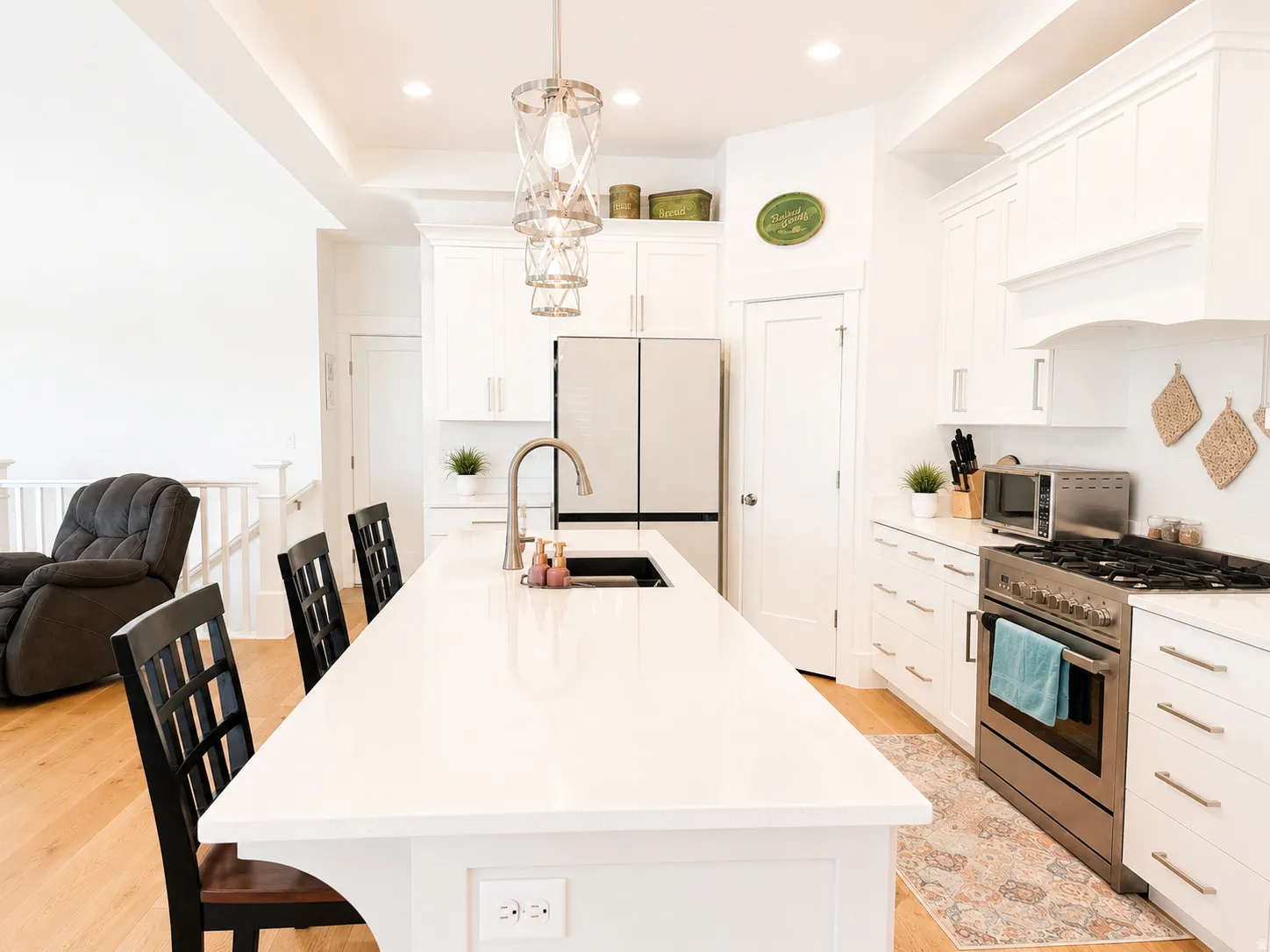 Contemporary kitchen featuring a large white countertop island, stainless steel appliances, white cabinetry with silver hardware, and wood-finish flooring