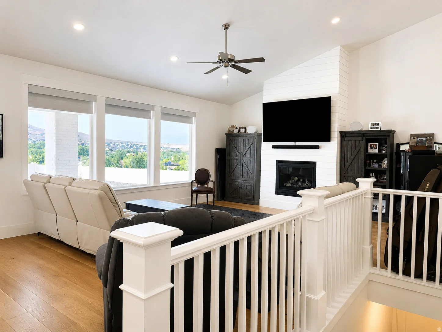Spacious living area featuring large windows, a fireplace with shiplap surround, wood-finish flooring, a ceiling fan, and recessed lighting