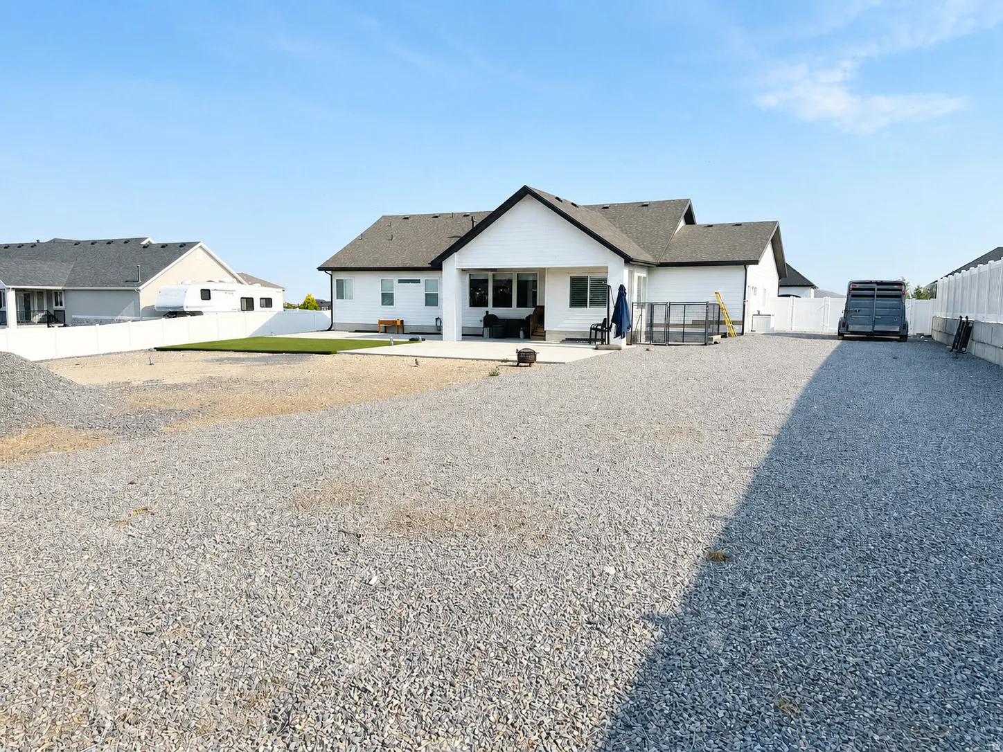 Expansive gravel lot featuring a white vinyl privacy fence, a concrete patio, and a section of artificial turf