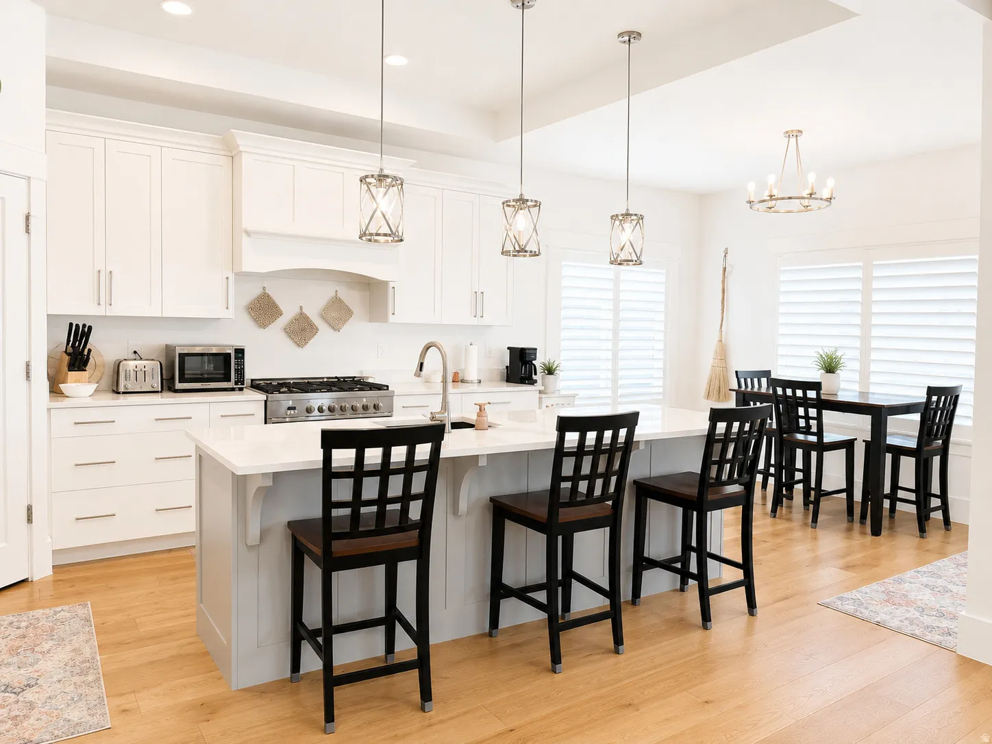 Open-concept kitchen featuring an expansive island with seating, stainless steel gas range, white cabinetry, and wood-finish flooring