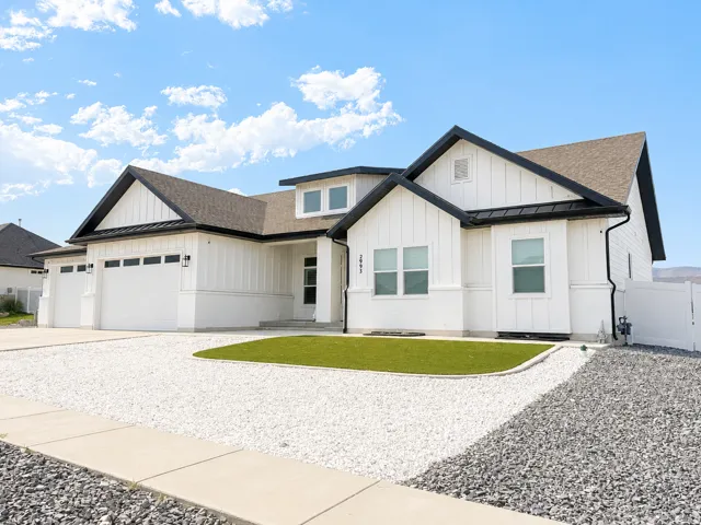 Modern farmhouse-style exterior featuring white vertical siding, dark trim, a two-car garage, a gravel driveway, and a manicured lawn