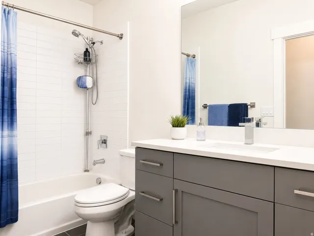 Contemporary bathroom featuring a tub/shower combination with white subway tile surround, a sleek toilet, a gray vanity with shaker-style cabinetry, and a countertop with an integrated sink and chrome faucet