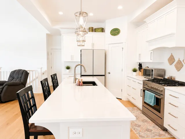 Contemporary kitchen featuring a large white countertop island, stainless steel appliances, white cabinetry with silver hardware, and wood-finish flooring