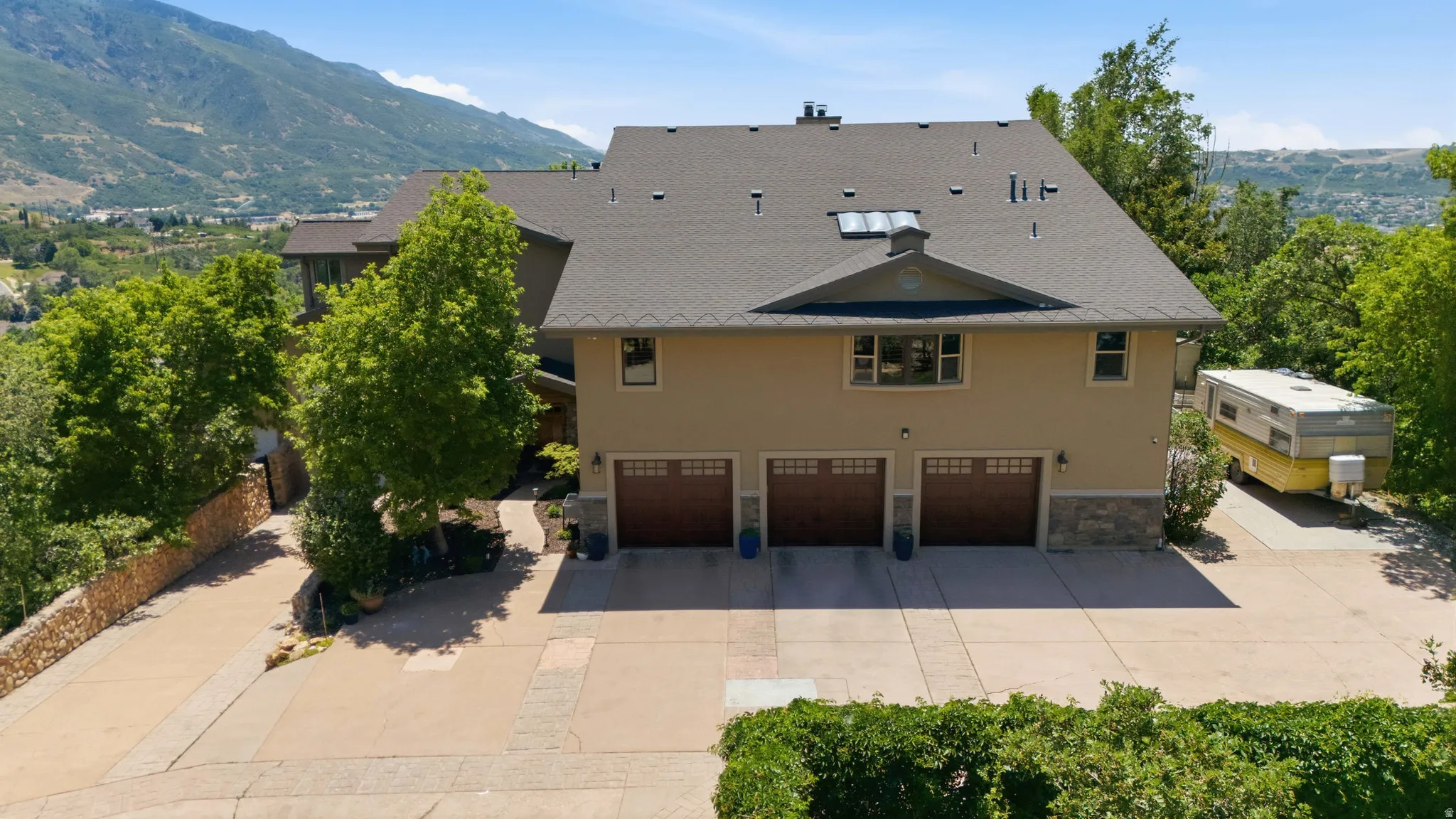 Multi-level stucco residence featuring a three-car garage with wood-finish doors, a stone facade accent, and a dark shingle roof