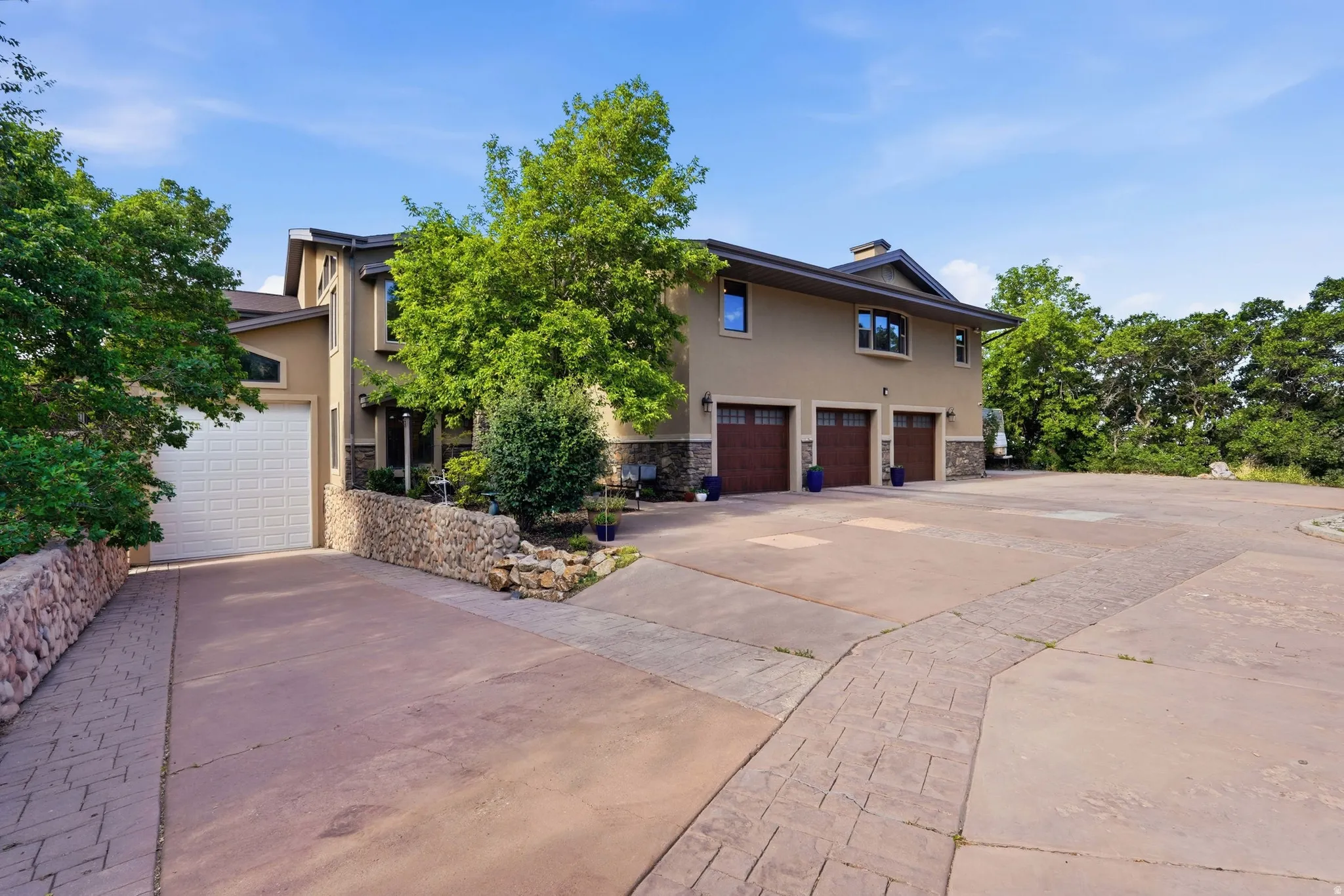 Stucco exterior featuring multiple garage bays, stone accents, and mature landscaping