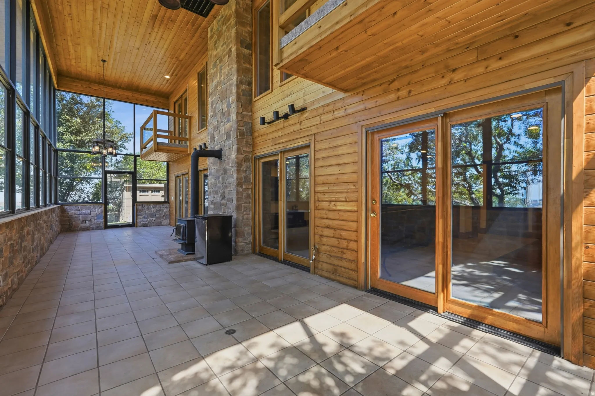 Spacious sunroom featuring full-wall windows, a wood-burning stove, and a stone accent wall