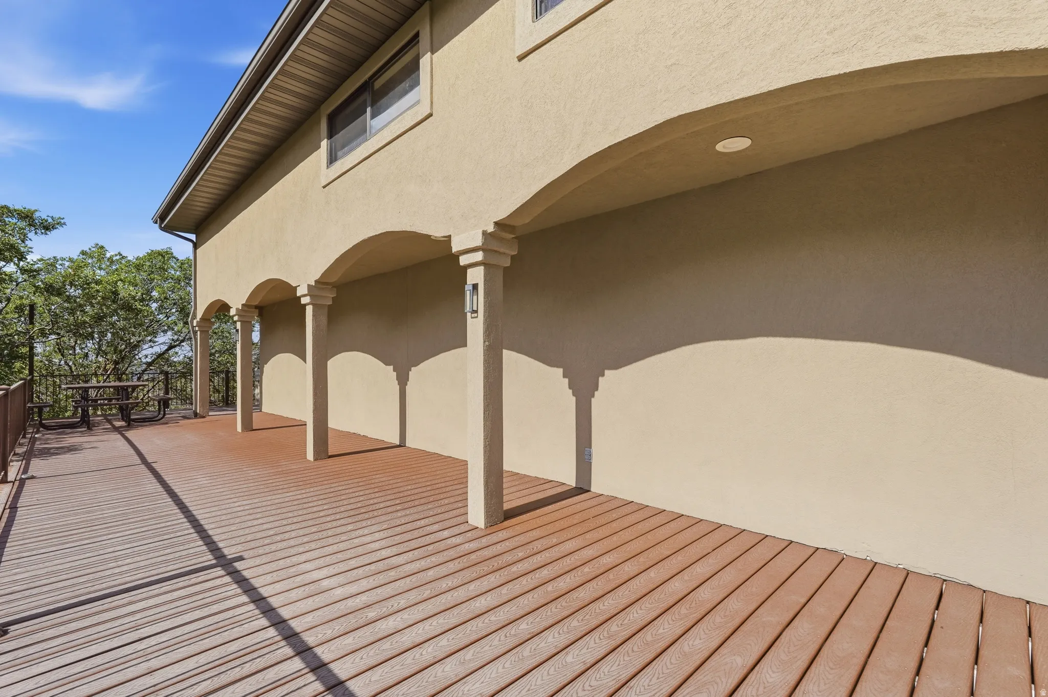 Spacious outdoor deck featuring wood-finish flooring, stucco exterior, multiple arched columns, recessed lighting, and a metal railing