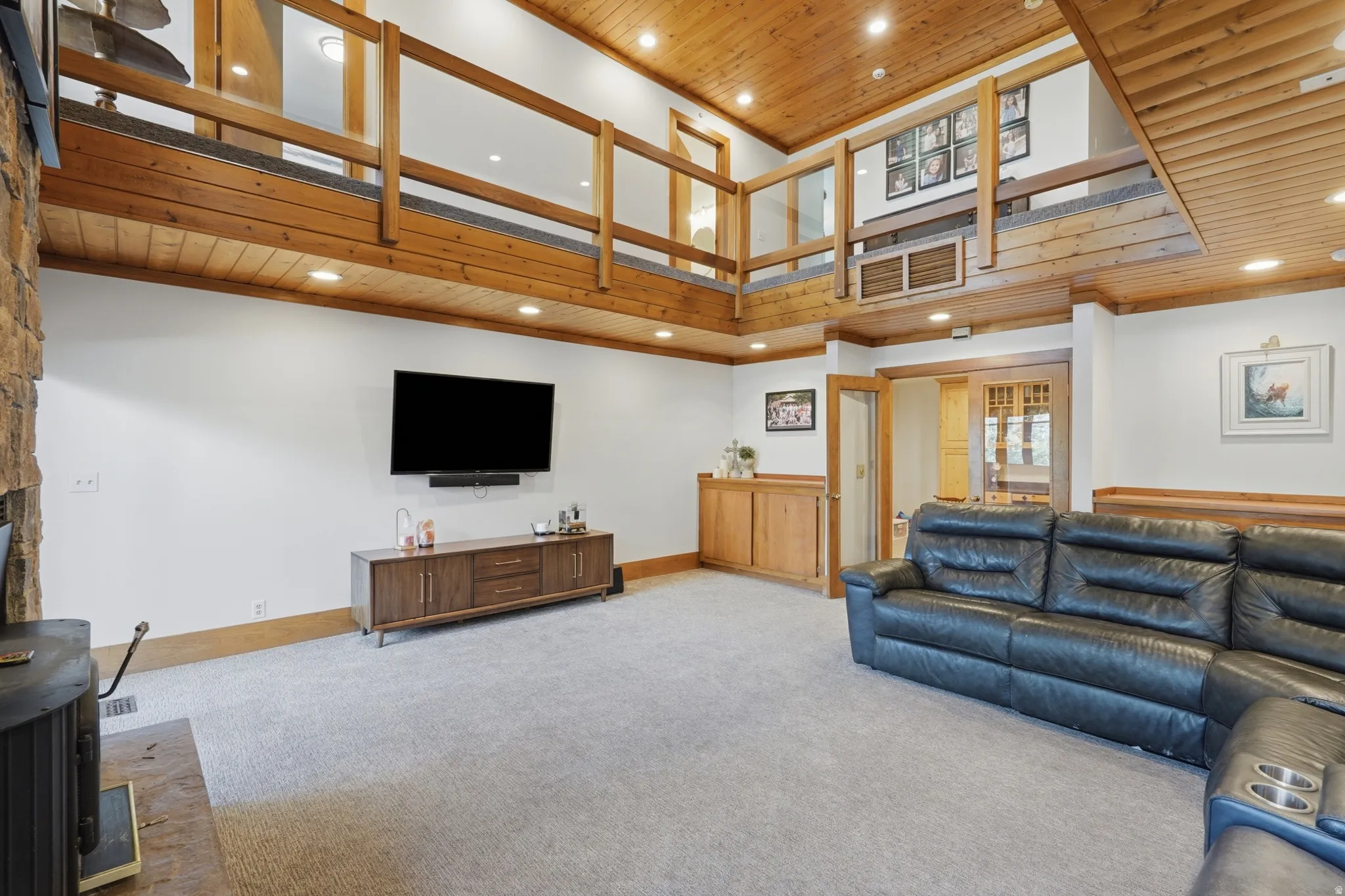 Vaulted ceiling with wood-finish paneling, an open lofted area with wood railings, and a stone-clad fireplace
