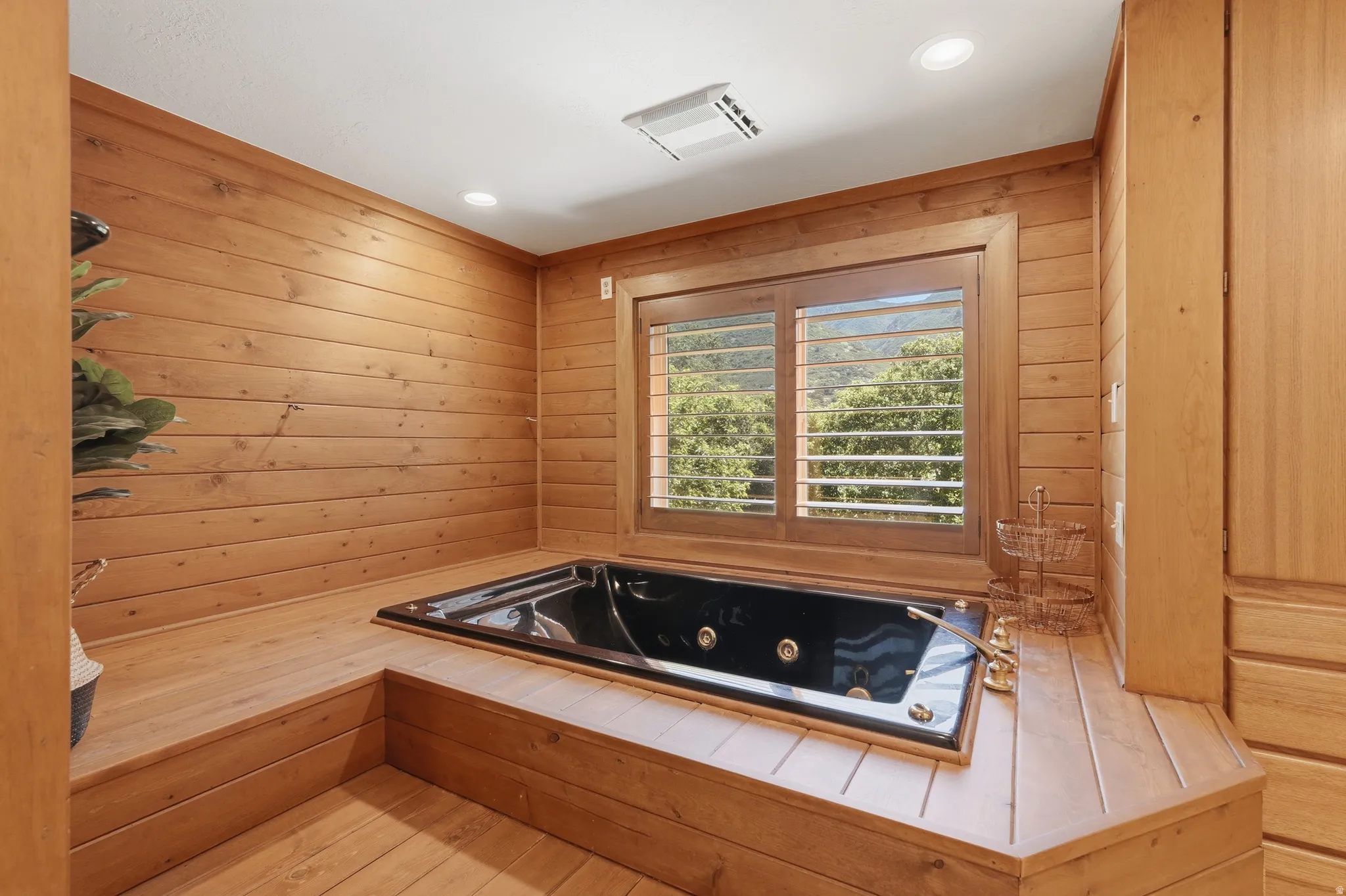 Built-in black soaking tub with gold-tone fixtures, surrounded by extensive wood paneling and wood-finish flooring