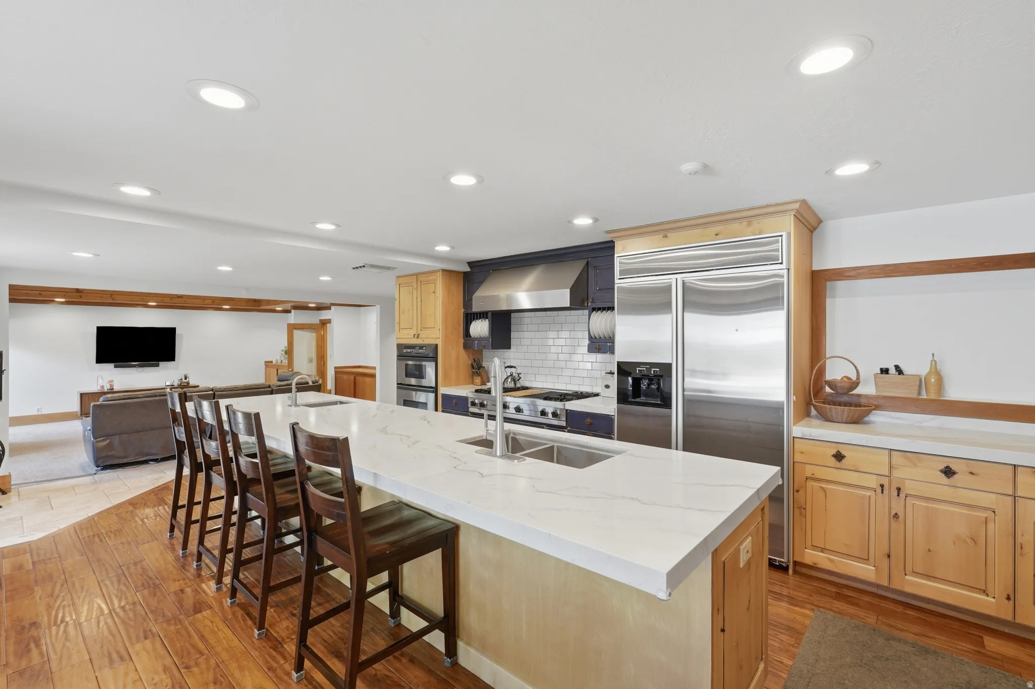 Kitchen featuring a large central island with seating, stainless steel appliances, white subway tile backsplash, and wood flooring