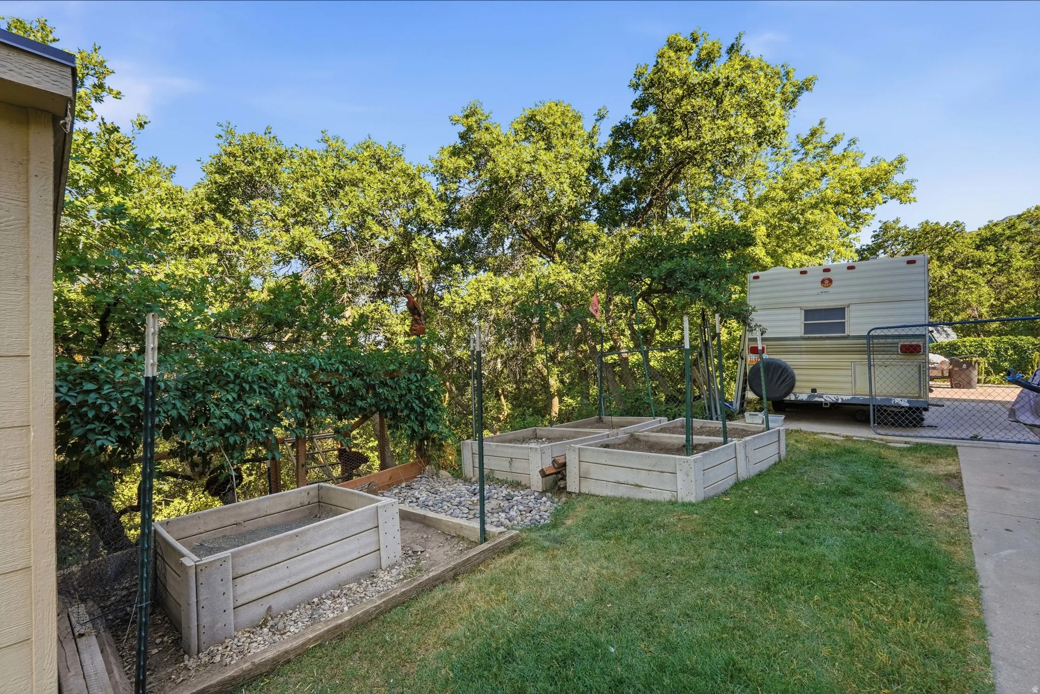 Rear yard featuring multiple raised garden beds, mature trees, and a concrete patio